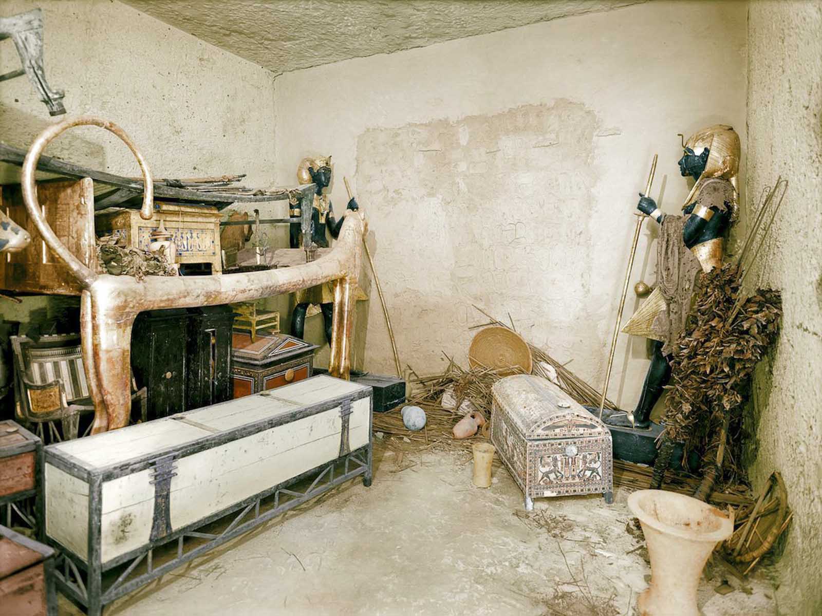A gilded lion bed, clothes chest and other objects in the antechamber. The wall of the burial chamber is guarded by statues.