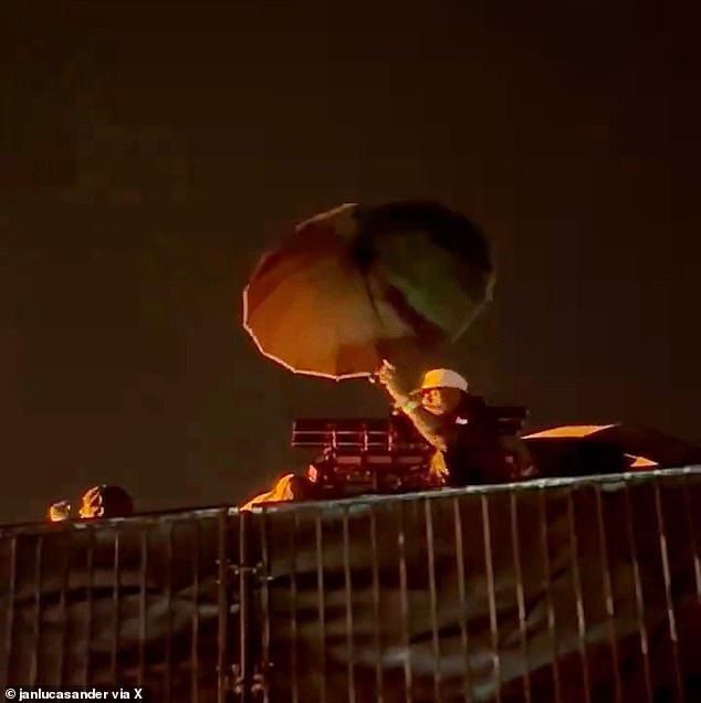 James held up an umbrella during Adele's performance on Thursday as he braved the rain