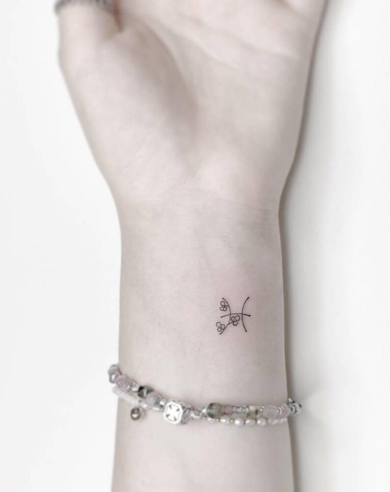 Minimalistic Pisces zodiac symbol with flowers tattooed on the wrist