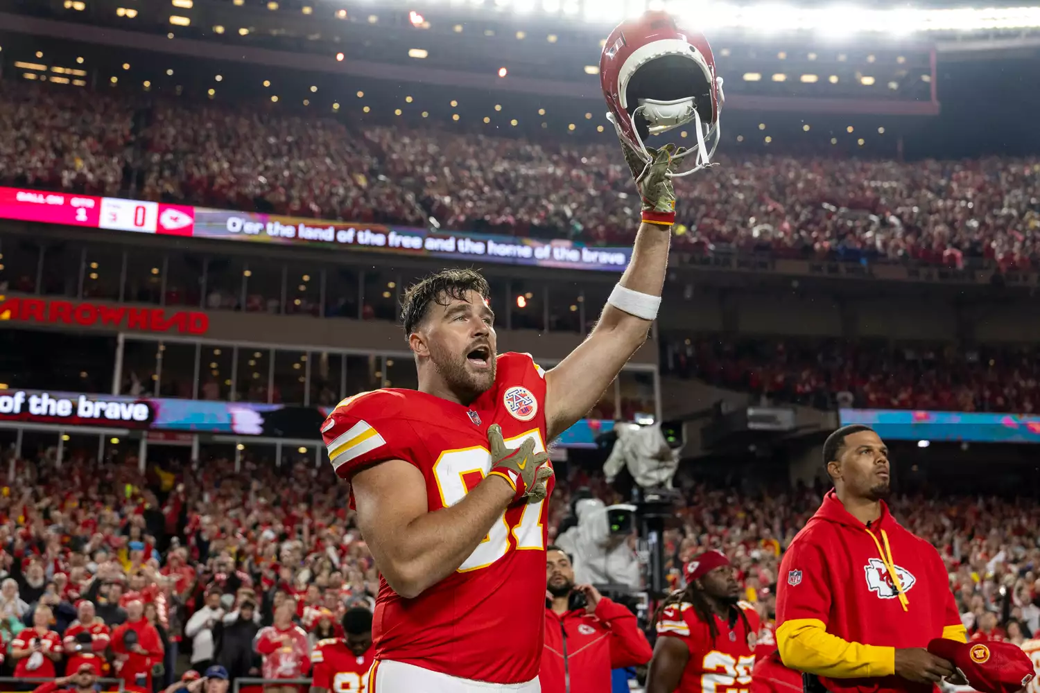 Travis Kelce #87 of the Kansas City Chiefs reacts as he raises his helmet during the national anthem prior to an NFL Football game against the Tampa Bay Buccaneers at GEHA Field at Arrowhead Stadium on November 04, 2024 in Kansas City, Missouri