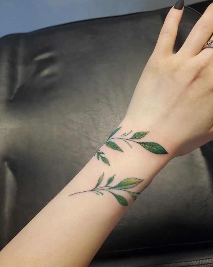 This may contain: a woman's hand with a green leaf tattoo on her left arm and wrist