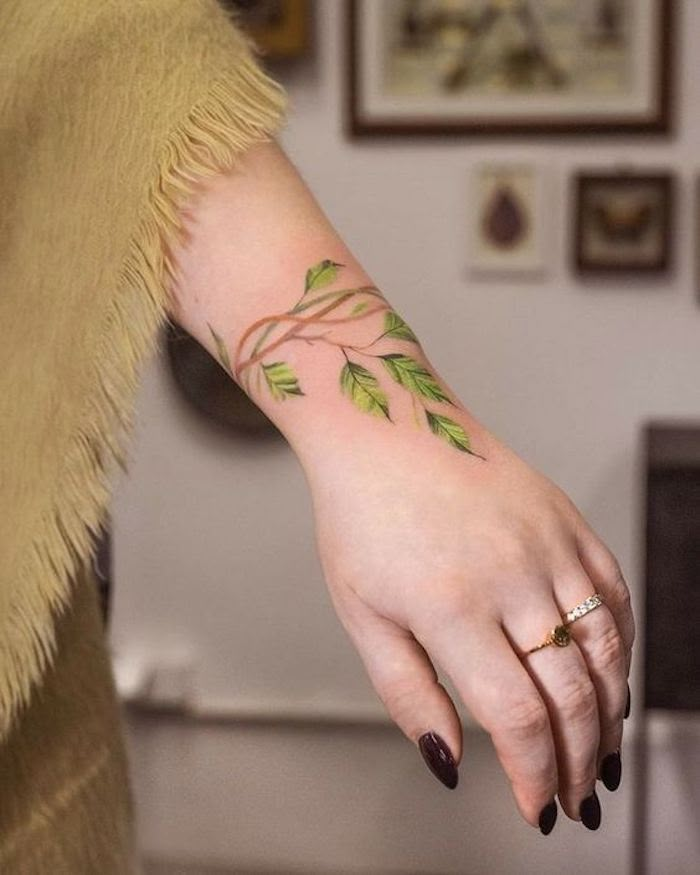 This may contain: a woman's hand with a green leaf tattoo on her left arm and wrist