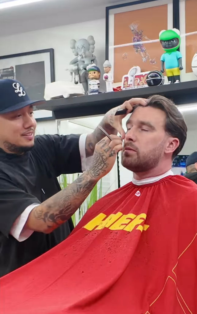 A close up of Travis Kelce getting his hair cut. The barber is using a razor to shape up his sideburns.