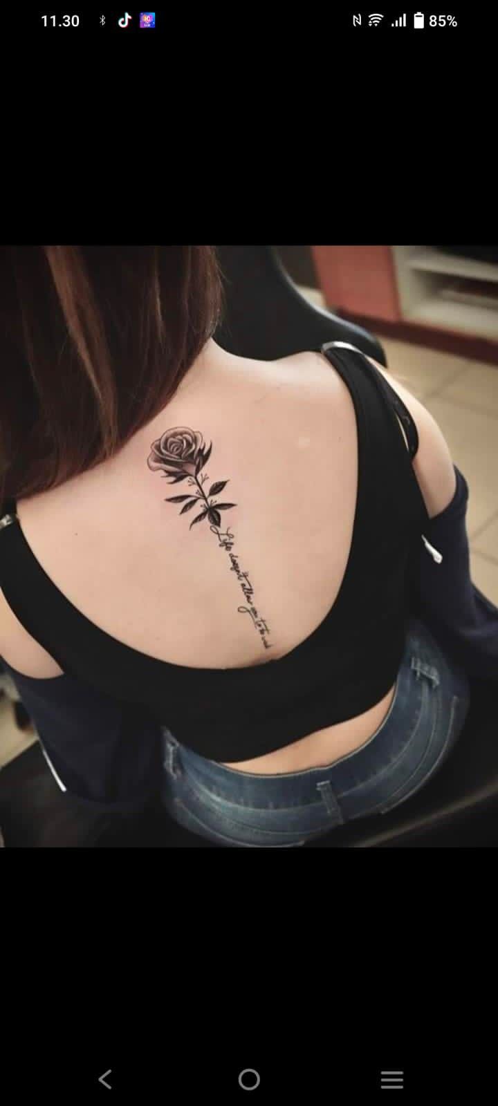 This may contain: the back of a woman's shoulder with a rose tattoo on her left side