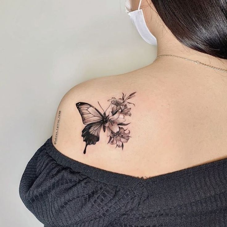 This may contain: a woman's shoulder with a butterfly and flowers tattoo on her upper arm,