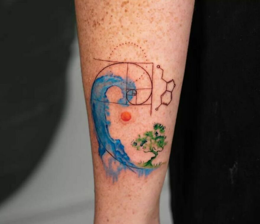 Watercolor tattoo on forearm featuring a blue wave, geometric lines, a tree, and a small orange sun. Watercolor tattoo on forearm featuring a blue wave, geometric lines, a tree, and a small orange sun.