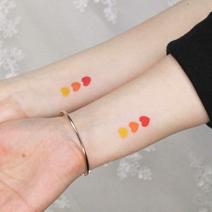 Colorful heart tattoos symbolizing family bonds on two wrists. Colorful heart tattoos symbolizing family bonds on two wrists.