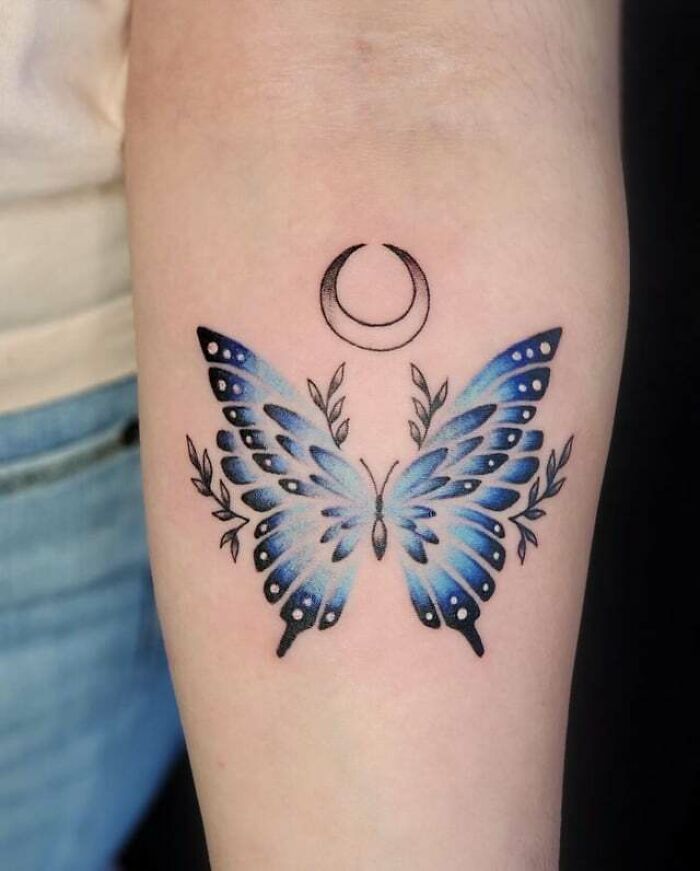 Colorful butterfly tattoo with crescent moon and leaf details on forearm. Colorful butterfly tattoo with crescent moon and leaf details on forearm.