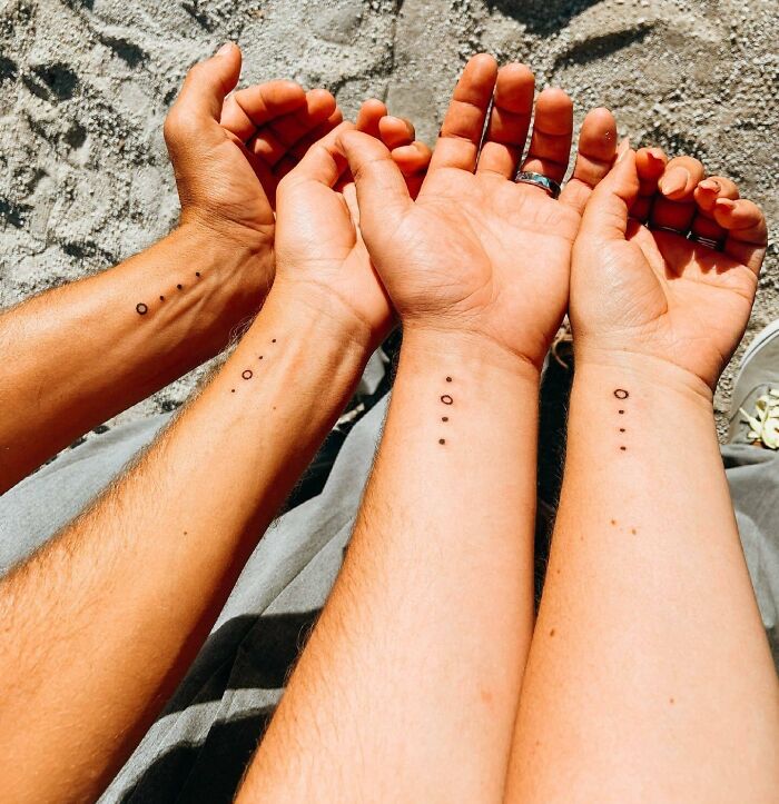Three forearms with matching minimal dot family tattoos symbolizing bonds. Three forearms with matching minimal dot family tattoos symbolizing bonds.