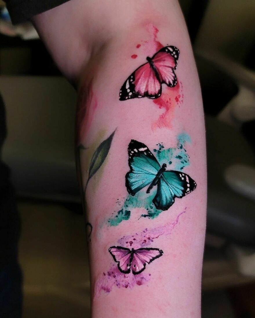 Arm with vibrant watercolor tattoo featuring pink and blue butterflies. Arm with vibrant watercolor tattoo featuring pink and blue butterflies.