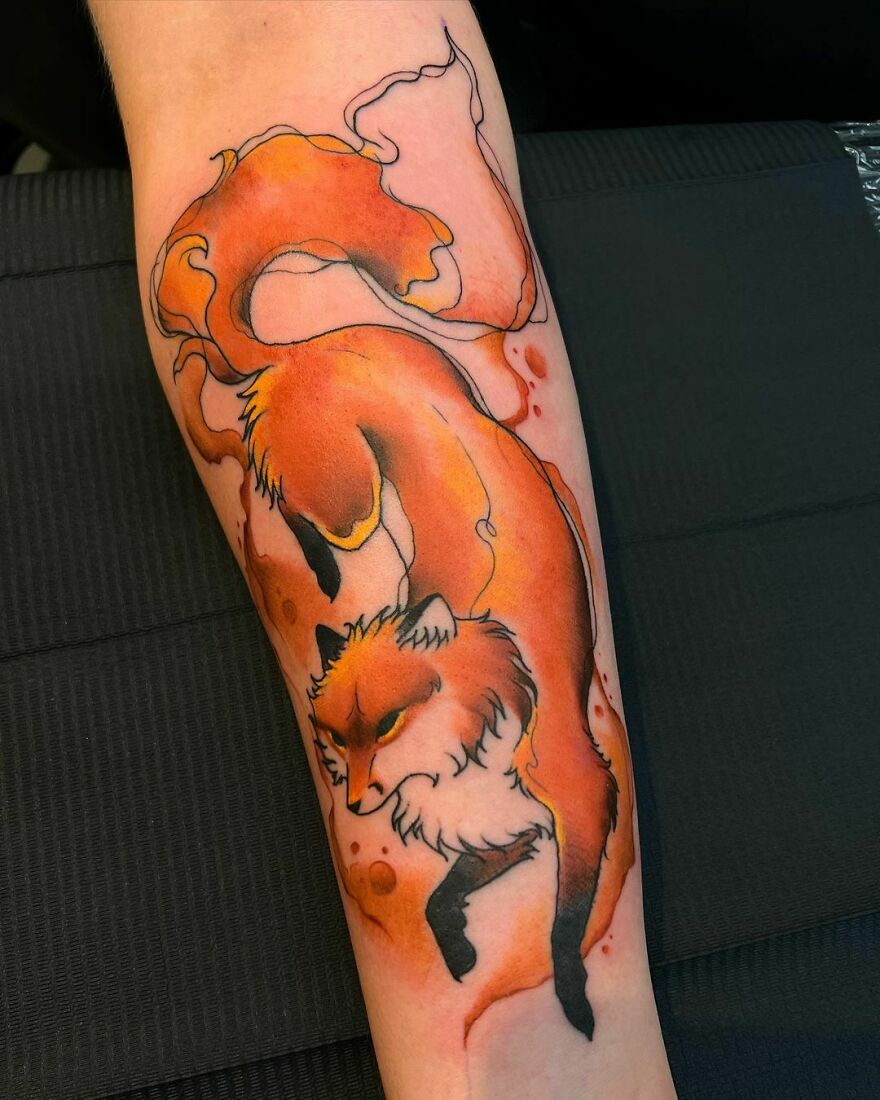 Watercolor tattoo of a vibrant orange fox with flowing ink style on the forearm. Watercolor tattoo of a vibrant orange fox with flowing ink style on the forearm.