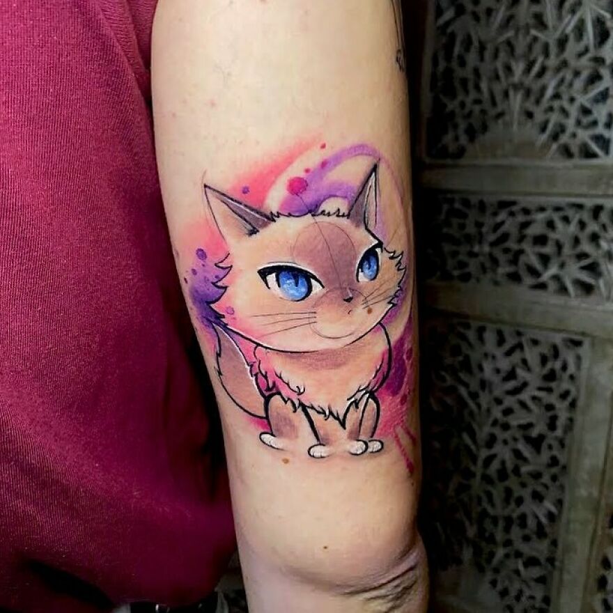 Watercolor tattoo of a cat with blue eyes on an arm, featuring pink and purple hues. Watercolor tattoo of a cat with blue eyes on an arm, featuring pink and purple hues.