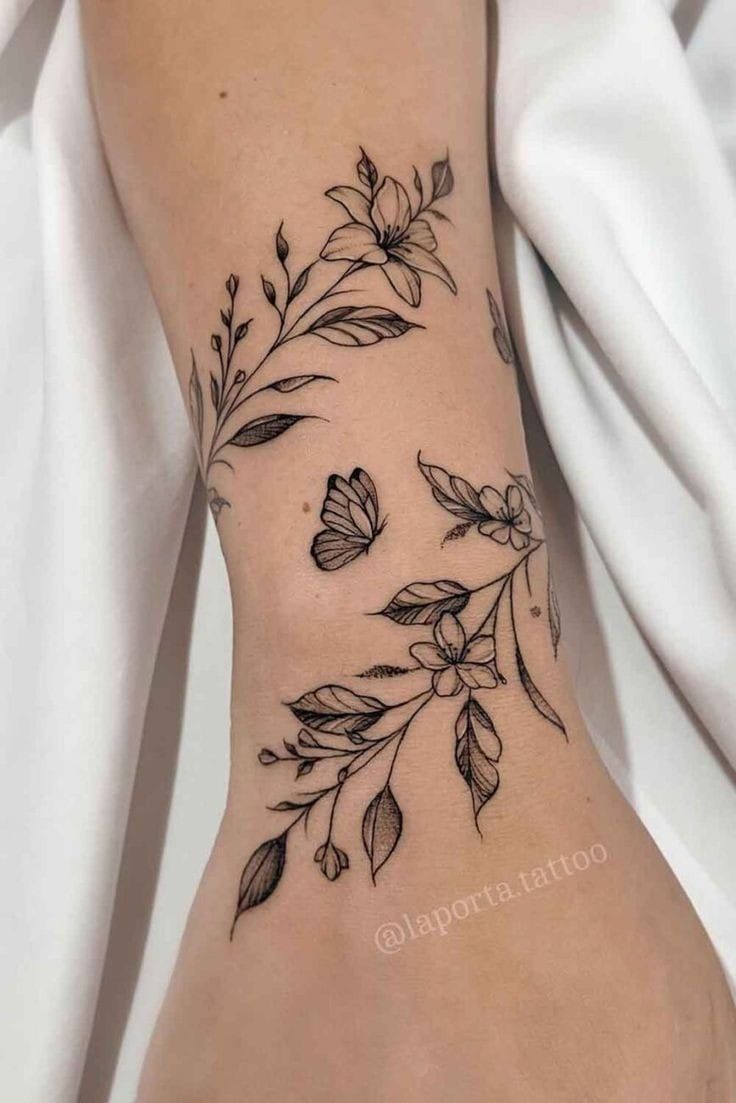 This may contain: a woman's foot with flowers and leaves tattooed on the side of her leg