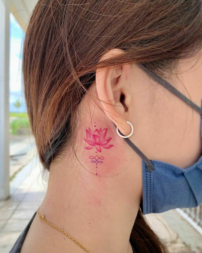 Delicate pink lotus flower tattoo behind ear, showcasing elegance and beauty. Delicate pink lotus flower tattoo behind ear, showcasing elegance and beauty.
